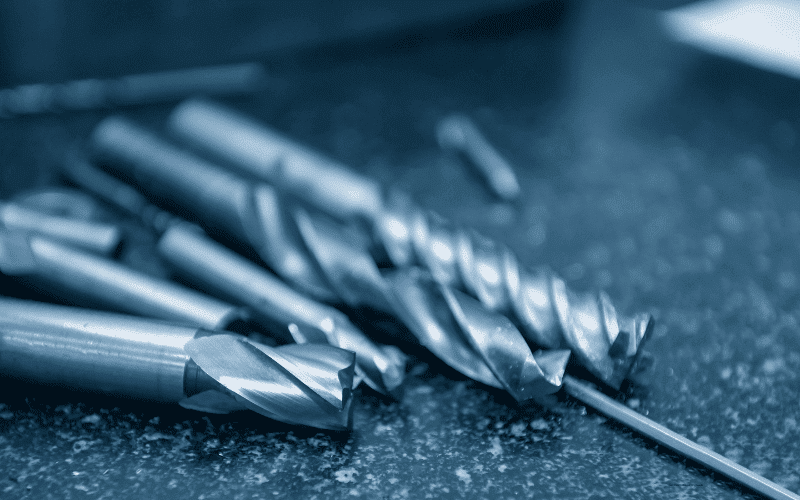 Close-up of various solid carbide cutting tools, including end mills and drills, laid out on a dark, textured surface.